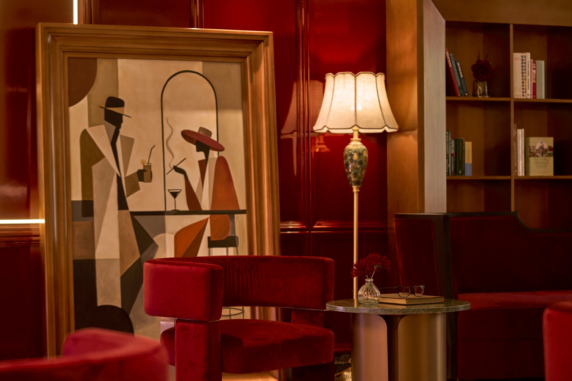 Ghế nhung đỏ và đèn cây cạnh bức tranh art deco, trên nền tường sơn mài đỏ.