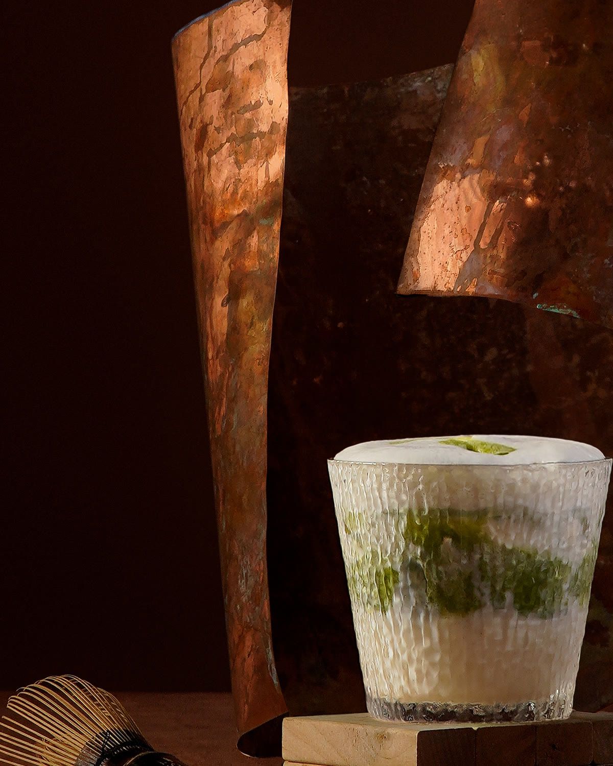 Ly matcha latte phủ lớp bọt, bên cạnh là chiếc chổi tre đánh trà.