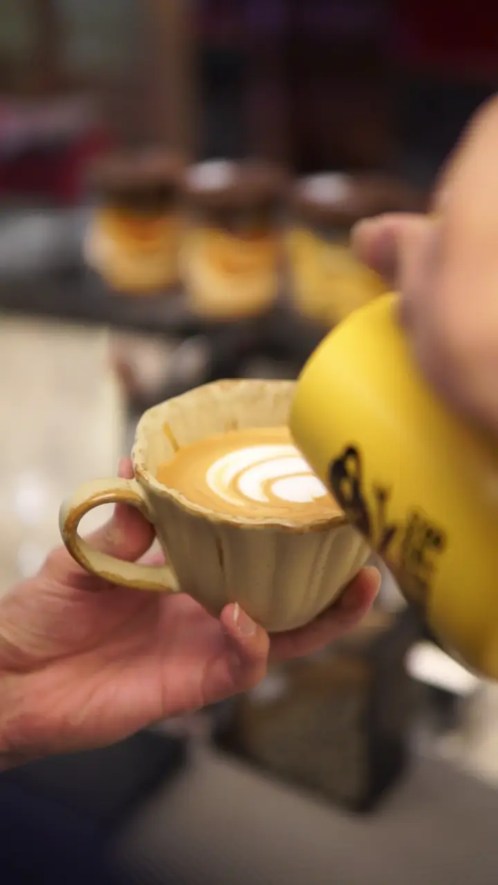 A barista at the Atelier bar tamps the coffee, steams milk, pulls an espresso and pours latte art.